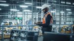 African American Engineer Using Laptop and Looking Out of the Office at a Car Assembly Plant. Vehicle Factory Line Operator Working on Computer, Overviewing Autonomous Electric Car Production.