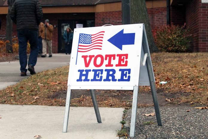 Vote Here Sign in Minneapolis on Election Day by Jasmine Webber of Mshale Newspaper Vote Here sign outside a Minneapolis polling location as people walk toward the building during a previous election